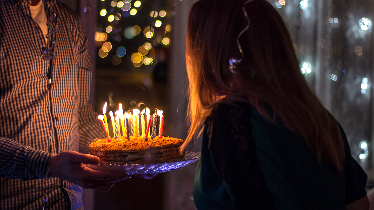 Happy birthday written in lit candles on colorful cake