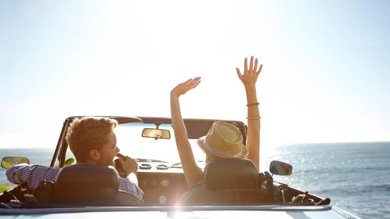 young couple parked by the ocean in a convertible on a sunny day