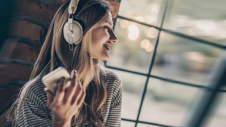 Happy woman listening music on headphones by the window